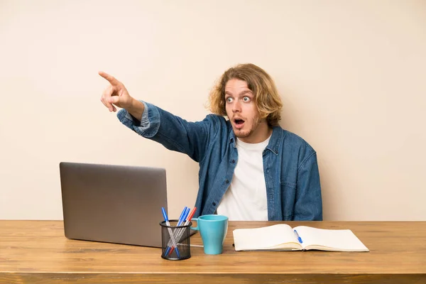 Blonde man with a laptop pointing away