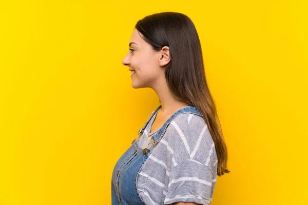 Junge Frau Latzhose Über Isoliertem Gelben Hintergrund Der Zur Seite — Stockfoto