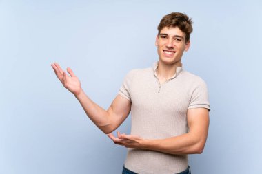 Izole mavi duvar üzerinde yakışıklı genç adam gelmeye davet için yan ellerini uzatıyor