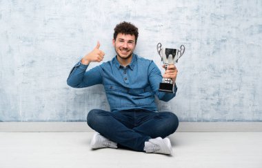 Yerde oturan genç adam elinde bir kupayla