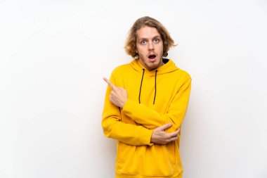 Beyaz duvar üzerinde sweatshirt ile Sarışın adam şaşırttı ve yan işaret