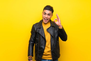 Izole sarı arka plan üzerinde genç adam şaşırttı ve ok işareti gösteren