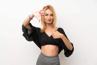 Izole beyaz duvar üzerinde genç sarışın kadın iyi-kötü işareti yapıyor. Evet ya da değil arasında kararsız