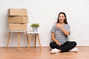 Yeni evde hareket eden genç kadın kutuların arasında parmağını yana doğru gösteren