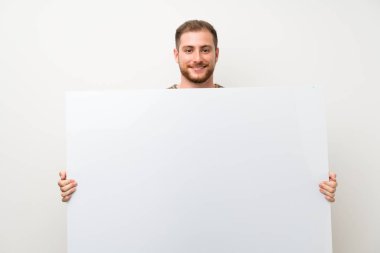 İzole beyaz duvar üzerinde yakışıklı adam eklemek için boş bir beyaz plasard tutan bir kavram