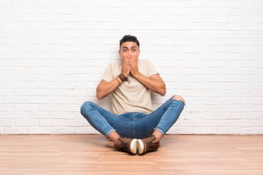 Genç bir adam yerde oturuyor ve yüzünde sürpriz bir ifade var.