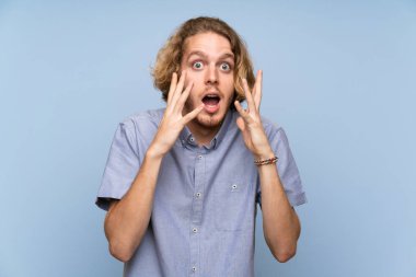 Sarışın adam sürpriz yüz ifadesi ile izole mavi duvarın üzerinden