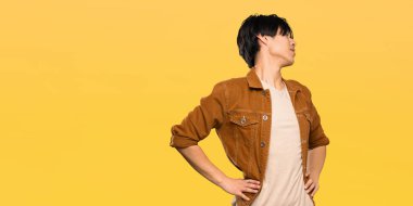 Izole sarı arka plan üzerinde bir çaba yapmış olduğu için sırt ağrısı muzdarip kahverengi ceketli Asyalı adam