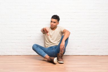 Yerde oturan genç adam başparmak aşağı işareti gösteren