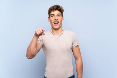 Izole mavi duvar üzerinde Yakışıklı genç adam şaşırttı ve ön işaret