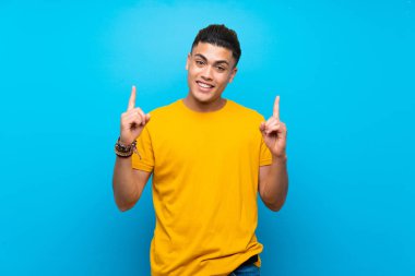 Izole mavi arka plan üzerinde sarı gömlek li genç adam harika bir fikir işaret