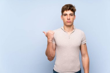 Izole mavi duvar üzerinde Yakışıklı genç adam mutsuz ve yan işaret