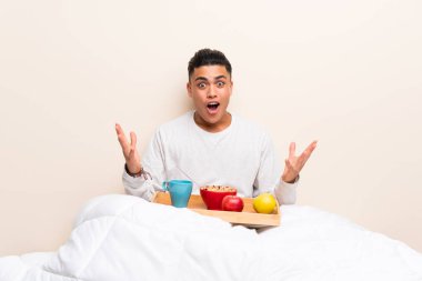 Sürpriz yüz ifadesi ile yatakta kahvaltı genç adam