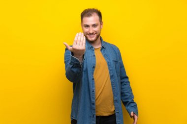 Sarışın adam izole sarı duvar üzerinde el ile gelmeye davet ediyor. Geldiğin için mutluyum.