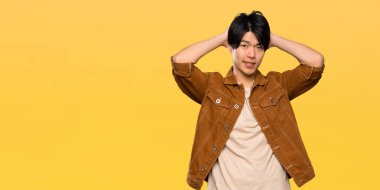 Kahverengi ceketile Asyalı adam sinirli ve izole sarı arka plan üzerinde baş ellerini alır