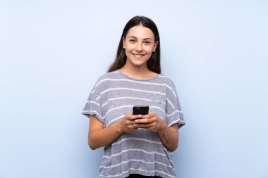 Cep telefonu kullanarak izole mavi arka plan üzerinde genç esmer kadın