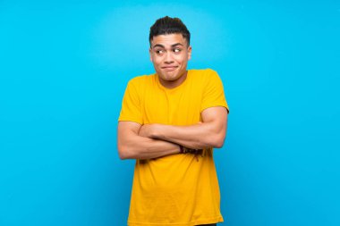 Izole mavi arka plan üzerinde sarı gömlekli genç adam omuzları kaldırırken şüphe jest yapma