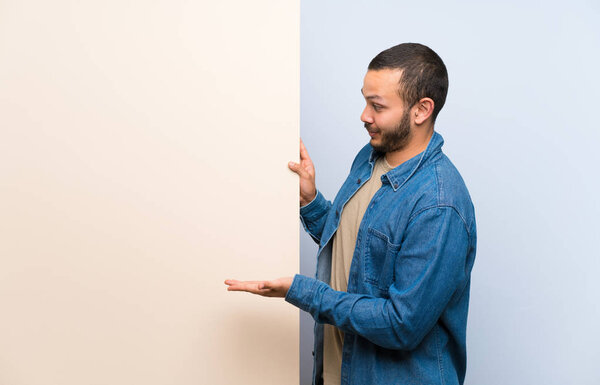 Colombian man holding an empty placard extending hands to the side for inviting to come