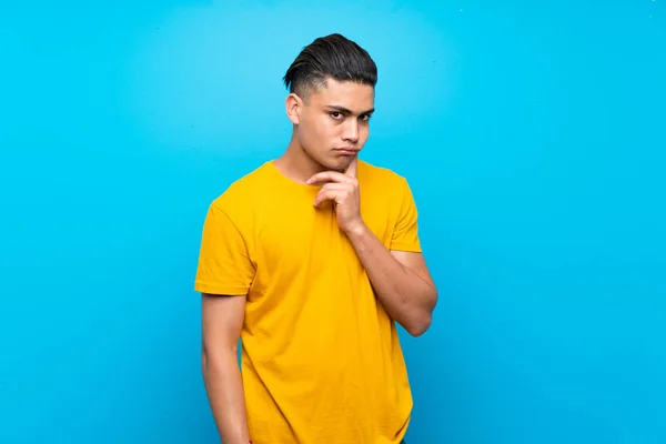 Jonge Man Met Geel Shirt Geïsoleerde Blauwe Achtergrond Zoek Naar — Stockfoto