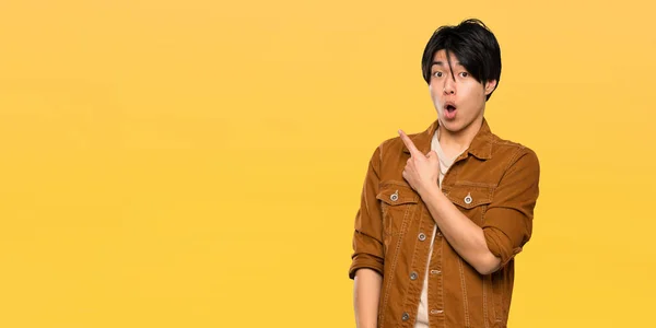 Asian Man Brown Jacket Surprised Pointing Side Isolated Yellow Background — Stock Photo, Image