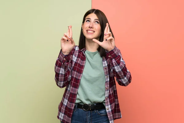 Young woman over isolated colorful wall with fingers crossing and wishing the best