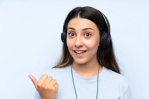 Mladá Žena Naslouchající Hudbě Přes Izolované Modré Pozadí Ukazující Stranu — Stock fotografie