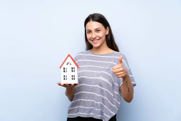 Joven Morena Sobre Fondo Azul Aislado Sosteniendo Una Casita —  Fotos de Stock