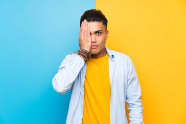 Elle bir göz kapsayan izole renkli arka plan üzerinde genç adam