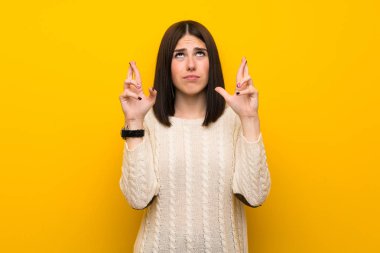 Parmakları geçerken izole sarı duvar üzerinde genç kadın geçiş ve en iyi dilek