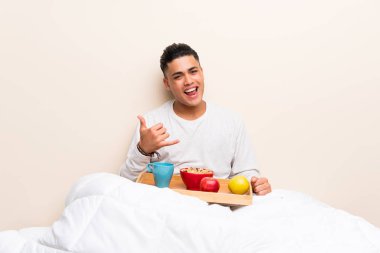 Yatakta telefon jesti yapan kahvaltı yapan genç adam