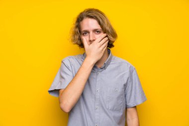 Elleriyle ağız kapsayan izole sarı arka plan üzerinde Blonde adam