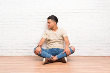 Genç adam yerde oturuyor, yan tarafa bakıyor.