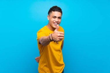 Iyi bir şey oldu çünkü başparmak ile izole mavi arka plan üzerinde sarı gömlekli genç adam