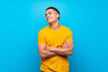 Izole mavi arka plan üzerinde sarı gömlekli genç adam mutlu ve gülümseyerek