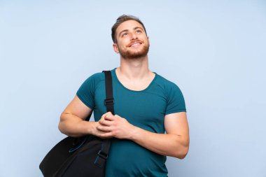 Mavi duvar üzerinde Sarışın spor adam gülümseyerek yukarı bakıyor