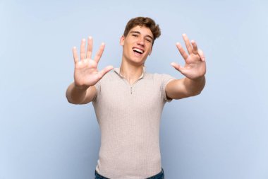 Izole mavi duvar üzerinde yakışıklı genç adam parmakları ile dokuz sayma