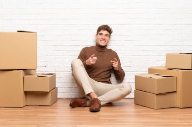 Yakışıklı genç adam kutuları arasında yeni bir evde hareket size parmak işaret