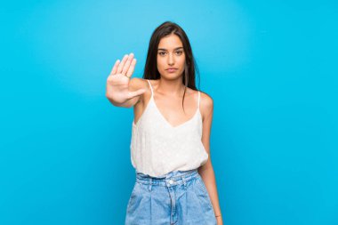 Soyutlanmış mavi arka plan hareketlerini durduran genç bir kadın.