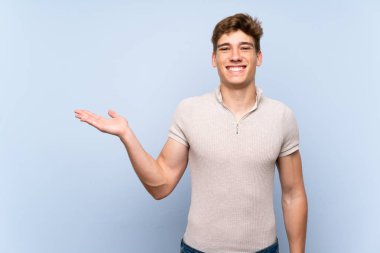 Bir reklam eklemek için avuç üzerinde copyspace hayali tutan izole mavi duvar üzerinde Yakışıklı genç adam