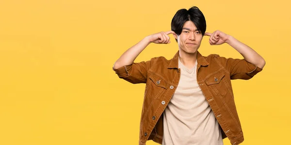 Asian Man Brown Jacket Frustrated Covering Ears Isolated Yellow Background — Stock Photo, Image