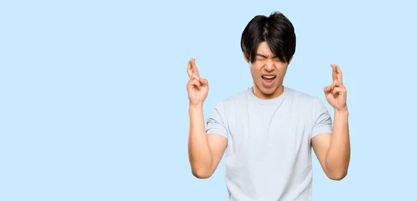 Asian Man Blue Shirt Fingers Crossing Isolated Blue Background — Stock Photo, Image