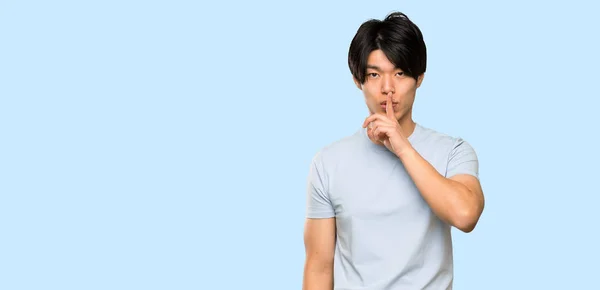孤立した青い背景の上に口に指を入れて沈黙のジェスチャーの兆候を示す青いシャツを持つアジアの男性 — ストック写真