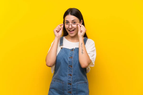 Gözlüklü Izole Sarı Arka Plan Üzerinde Dungarees Genç Kadın Şaşırttı — Stok fotoğraf