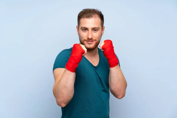 Blonde sport man over blue wall in boxing bandages