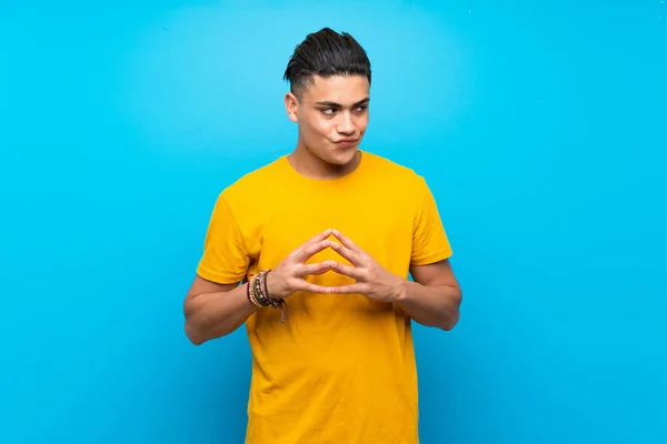 Young man with yellow shirt over isolated blue background scheming something