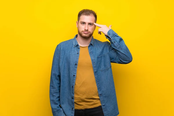 Blonde man over isolated yellow wall with problems making suicide gesture