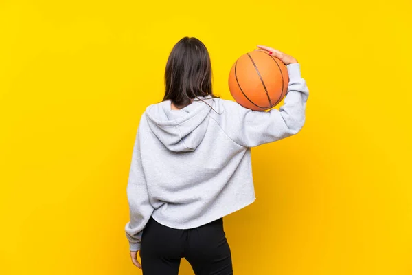 Νεαρή γυναίκα παίζει μπάσκετ πάνω από το απομονωμένο κίτρινο φόντο — Φωτογραφία Αρχείου
