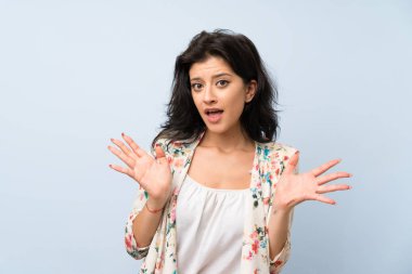 Soyutlanmış mavi arka planı olan genç bir kadın. Şaşırtıcı bir yüz ifadesi.