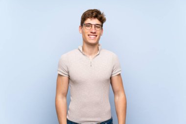 Gözlük ve mutlu izole mavi duvar üzerinde Yakışıklı genç adam