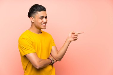Izole pembe duvar üzerinde sarı gömlek li genç adam yan parmak işaret